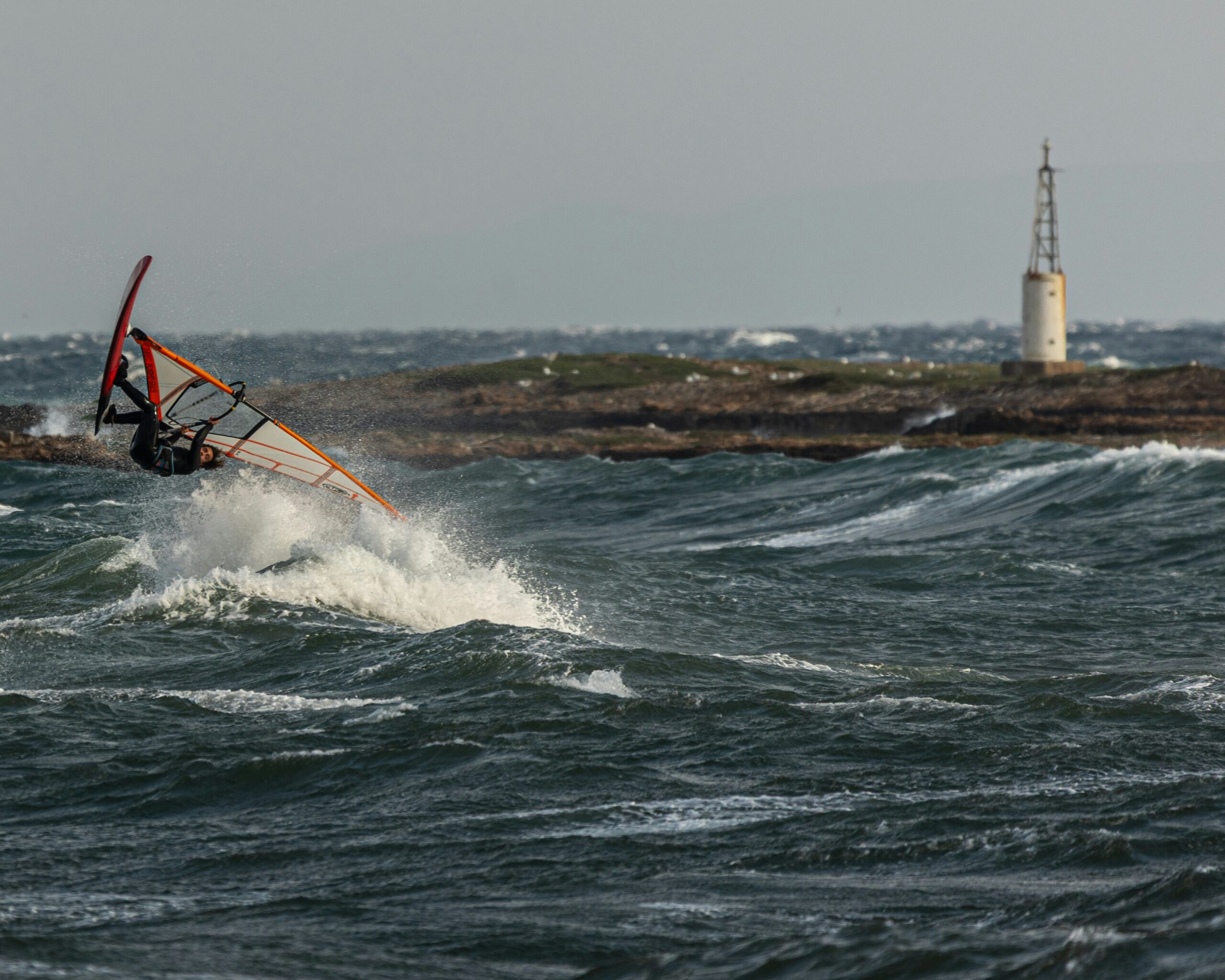 Windsurfer rides waves in choppy water near a lighthouse