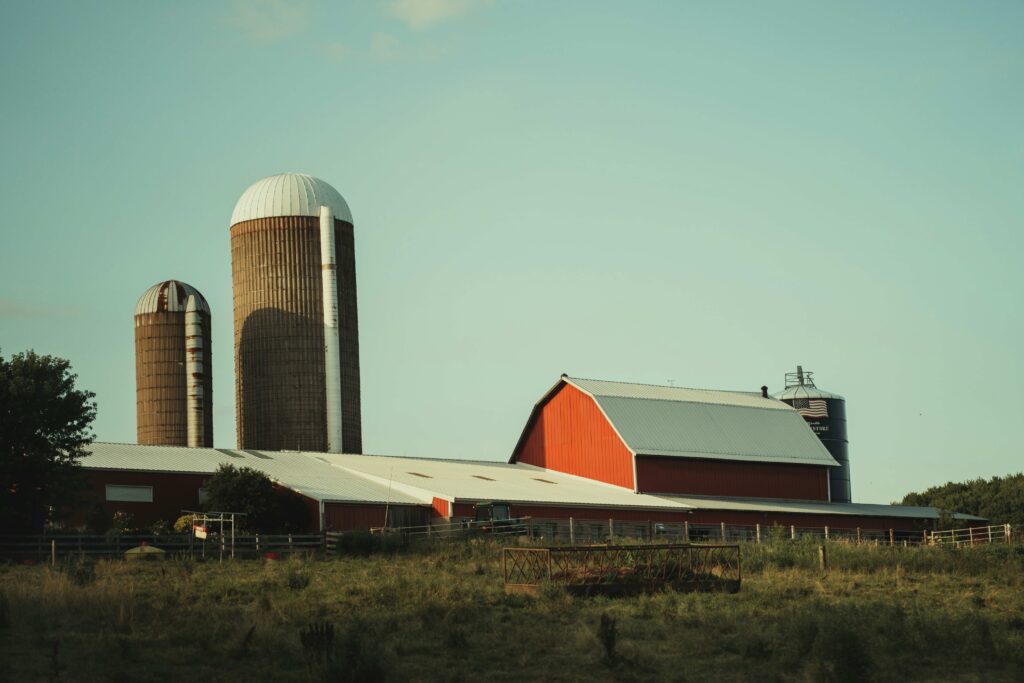 Red barn stands in the middle of a green farm field under a clear blue sky